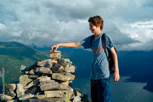 Smiling teenager adding a stone to a cairn with a scenic mountain landscape and lake in the background, Romsdalfjorden, Norway photo