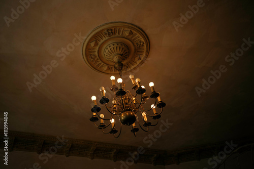 Anti0ue chandelier with candles lit against a ceiling with intricate mouldings in a dimly lit room, Poznan, Poland photo