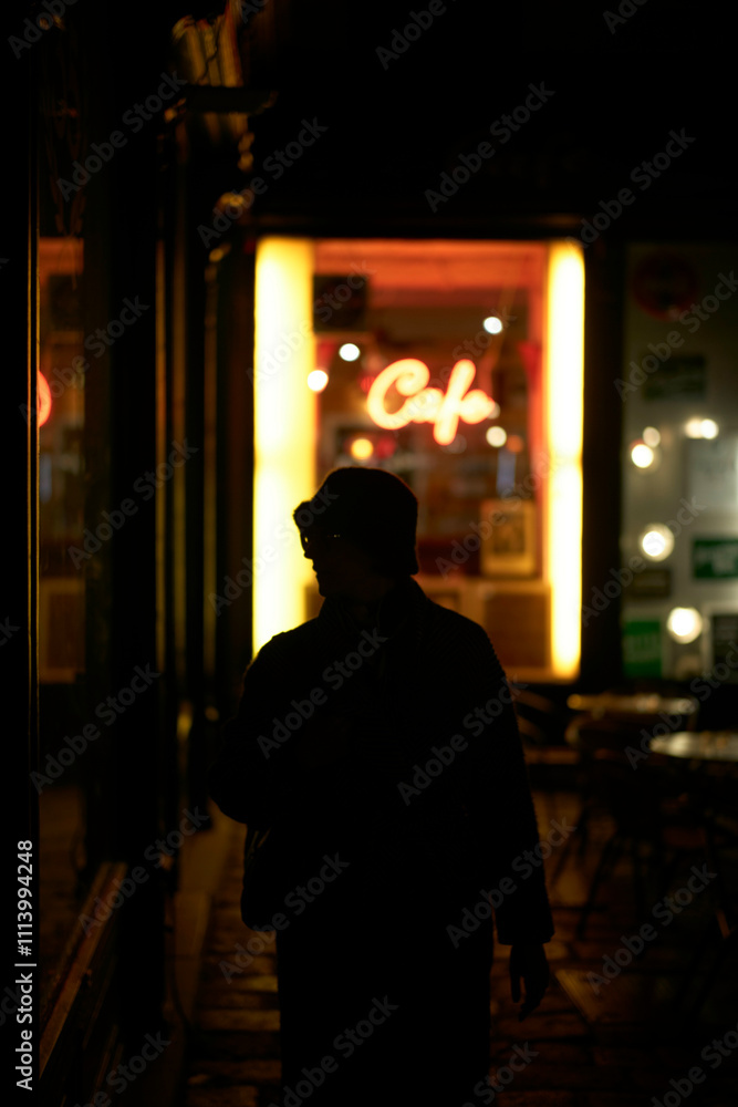 Silhouetted figure standing in front of a brightly lit cafe at night Silhouetted figure standing in front of a brightly lit cafe at night