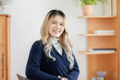 Smiling young woman with blonde highlights standing in a well-lit room with bookshelves in the background. photo