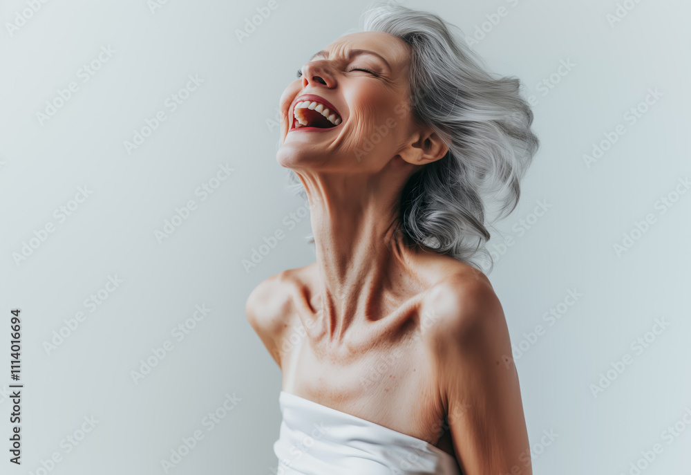 Fototapeta premium Joyful portrait of an elderly Caucasian woman with silver hair, laughing freely and exuding confidence, set against a minimalist white background