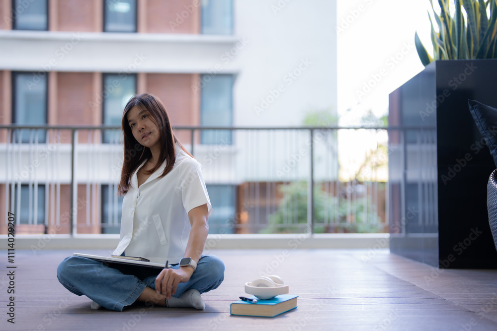 Young asian freelancer woman relaxing on the balcony after working on a tablet, enjoying the comfort of her smartwatch, headphones, and a book nearby, embracing a peaceful moment Young asian freelancer woman relaxing on the balcony after working on a tablet, enjoying the comfort of her smartwatch, headphones, and a book nearby, embracing a peaceful moment