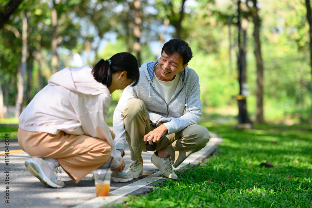 Caring young adult daughter tying her father shoelaces during their walk in the park Caring young adult daughter tying her father shoelaces during their walk in the park