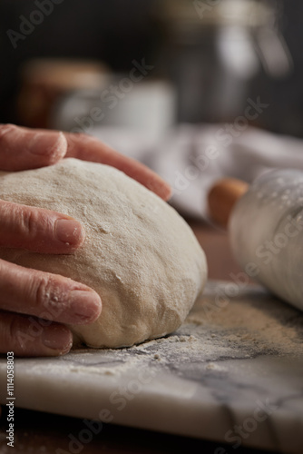 Cooking homemade bread. Sieving flour over raw bread dough rolled with rolling pin on marble board, dark background, selective focus. Baker hands on dough. photo