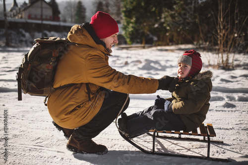 dad takes his 4 year old son sledding in winter on a frosty sunny day in a cottage village photo