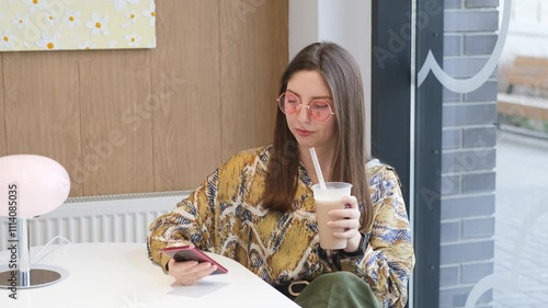 Pretty brunette with phone in hands relaxing in cafe. Woman drinking coffee cocktail