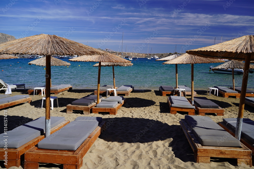 Fototapeta premium lounge beds and sunshades on Lindos bay sandy beach