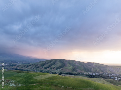 Drone view of mountains at sunset. A lot of clouds on the sky. The setting sun illuminates the valley and hillside fields. Evening landscape.