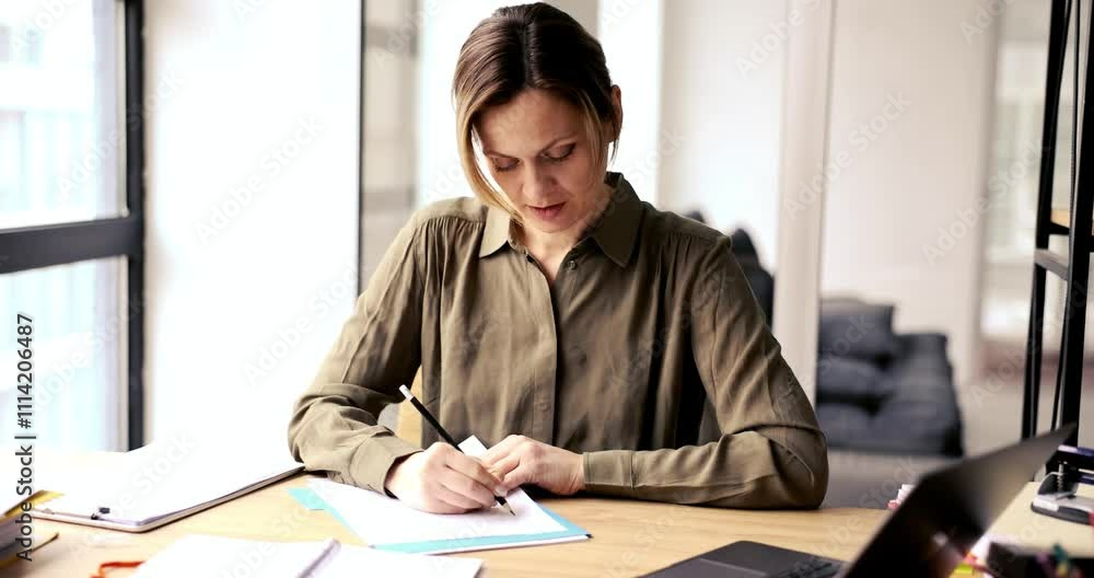 A woman focused and diligently writing detailed notes at a stylish modern office desk, enveloped by natural light A woman focused and diligently writing detailed notes at a stylish modern office desk, enveloped by natural light
