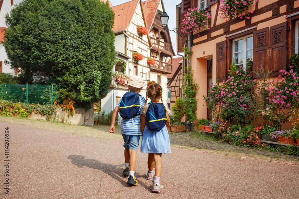 Obraz premium Two children walk holding hands through sunny village Eguisheim