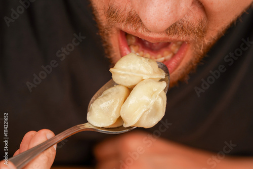 Man enjoying steamed dumplings, helping himself with a spoon. Great for cooking and lifestyle concepts.