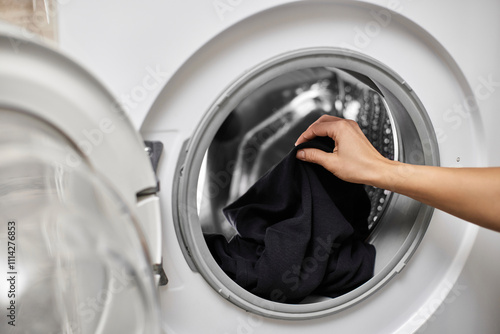 Woman putting black cotton clothes into the washing machine, close-up photo