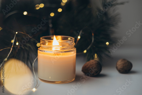 A burning candle, Christmas tree branches and hot lights of a garland. photo