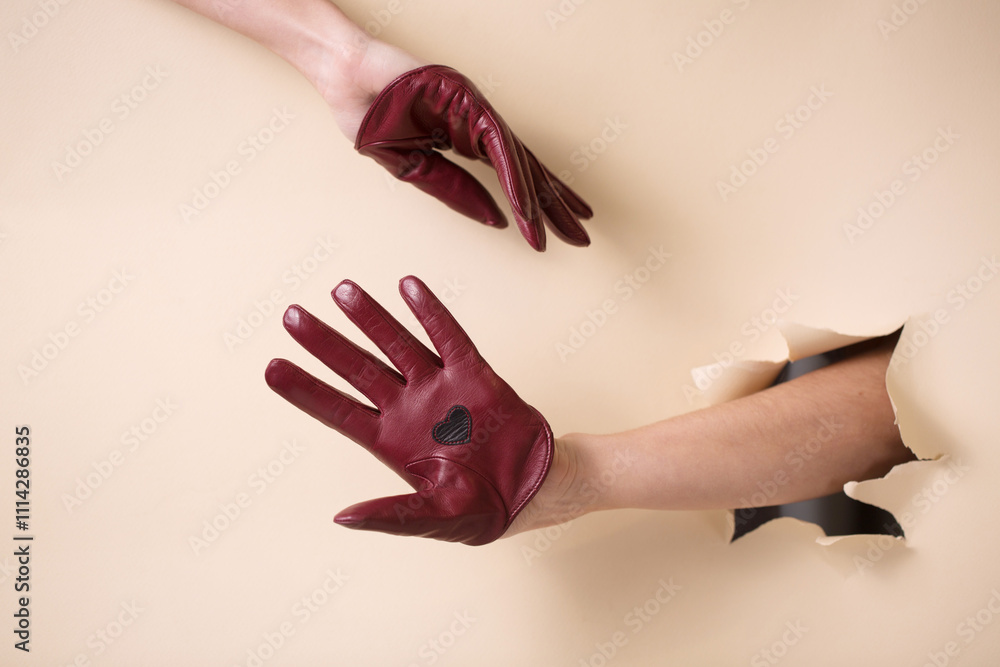 Two tender female hands in leather burgundy gloves on a beige paper background