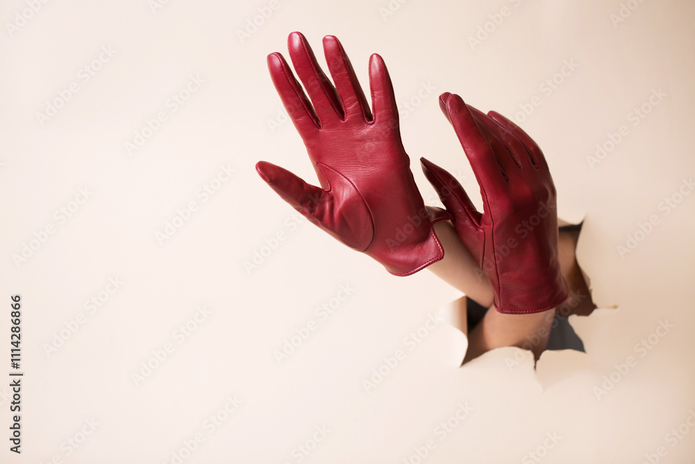 Two female hands in leather burgundy gloves on a beige paper background