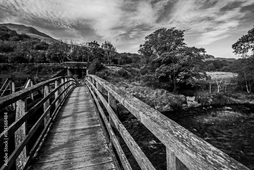 Dramatic Black and White view along a weathered Wooden Hiking bridge crossing the river Glaslyn in Eryri National Park in Wales.  photo