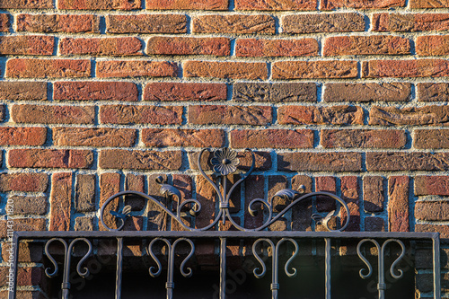 Backsteinmauer mit schmiedeeisernem Fenstergitter mit Schattenwurf im Streiflicht photo