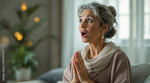 Excited Senior Woman with Gray Hair Expressing Joy and Surprise Indoors, Wearing Cozy Clothes in a Warmly Lit Living Room, Ideal for Holiday or Lifestyle Themes