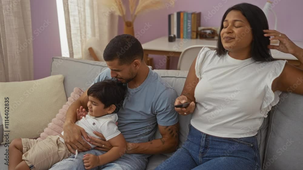 Family watching television on couch at home with man embracing boy and woman holding remote control Family watching television on couch at home with man embracing boy and woman holding remote control