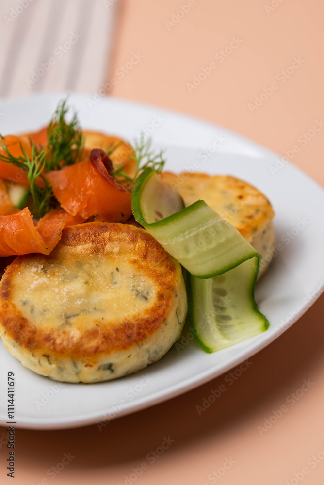 Syrniki with creamy cheese and dill, served on plate with fresh cucumber slices, thinly sliced smoked salmon, and herbs. Concept of traditional home recipes, and balanced meals. Syrniki with creamy cheese and dill, served on plate with fresh cucumber slices, thinly sliced smoked salmon, and herbs. Concept of traditional home recipes, and balanced meals.