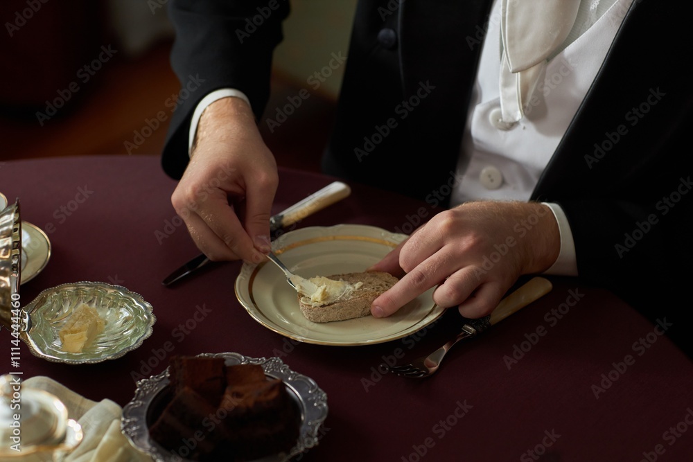 Top view closeup of young gentleman putting butter on slice of bread at richly set dining table with silver and china, copy space Top view closeup of young gentleman putting butter on slice of bread at richly set dining table with silver and china, copy space