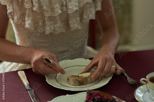 Top view closeup of classic young lady putting butter on slice of bread at richly set dining table with silver and china, copy space photo