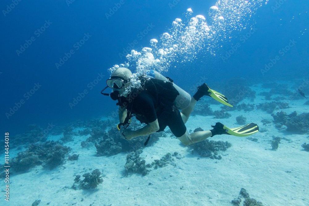 Single scuba diver with the equipment over colorful coral reef on the sandy bottom of tropical sea, underwater landcape
