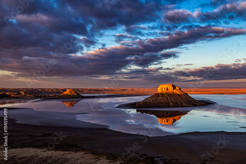 Kazakhstan, Ustyurt National Park, Karynzharyk. At dawn, 2 lonely mountains are surrounded by a thin layer of water with a perfect reflection. Clouds are illuminated by the sun from below