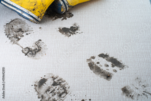 Yellow rubber boots create distinct muddy footprints on a light-colored textured surface, indicating a recent outdoor activity in wet conditions. photo