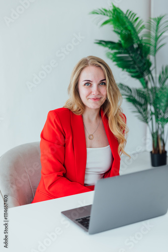 blonde woman in red business suit with laptop online in office at desk