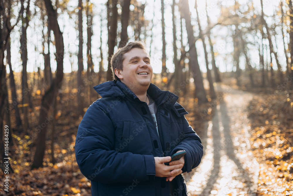 Adult 30s man hiker stand outdoors in a natural setting, smile while using his mobile phone outdoors. Hiking, lifestyle, adventure and tourism concept.