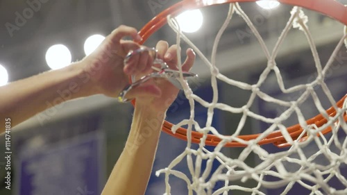 a closeup of a person's hand is seen cutting down a piece of the basketball net after winning a championship game