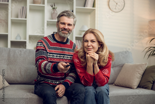 Gray-haired mature good-looking man switching on tv while sitting on a sofa with his wife