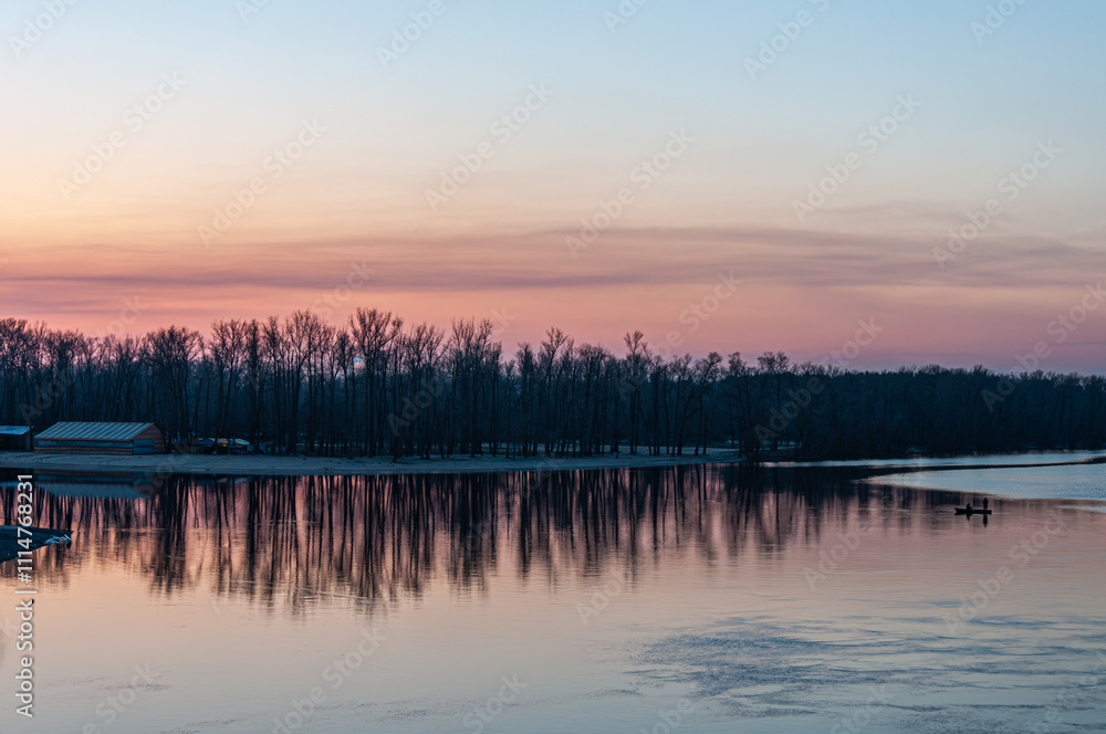 Obraz premium A tranquil winter view of the Dnipro River, showcasing its vast expanse under a serene sky, with faint silhouettes of Kyiv’s skyline and bridges in the distance.