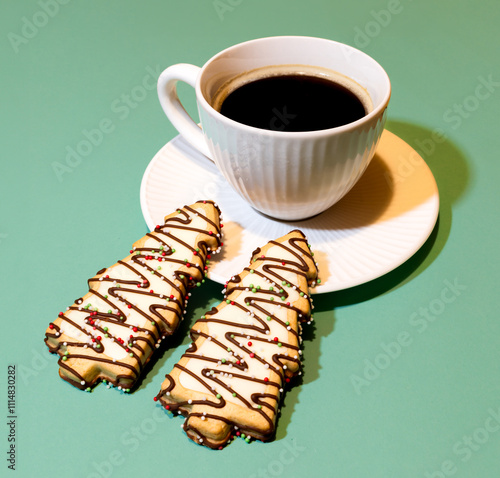 A cup of coffee and two chocolate cookies with green sprinkles on them. Christmas coffee break