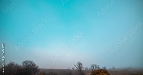 4k mountain meadow timelapse at the autumn sunrise time. Wild nature and rural haystacks on grass field. Morning fog, sun rays and trees. Motorised dolly slider