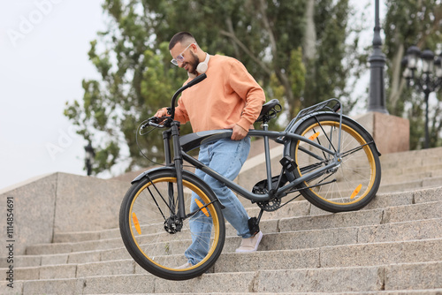 Fotografie Young happy man with headphones and bicycle going downstairs in city