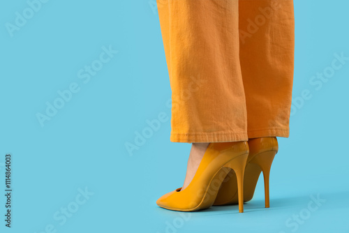 Legs of young woman in yellow high heels on blue background photo