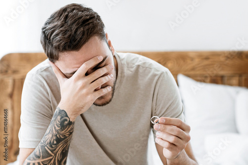 Crisis in marriage concept. Sad husband holds wedding ring in hand, offended turned away his wife on bed photo