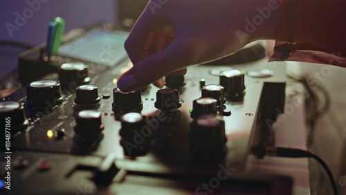 DJ hand tweaking knobs on mixer mixing music in clubbing scene closeup.  photo