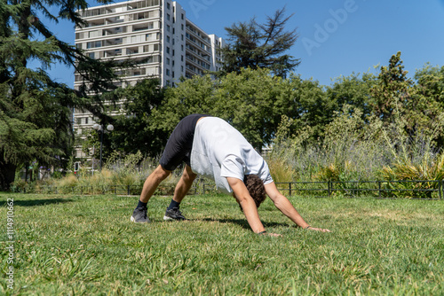 Obraz na płótnie A young man stretches in a sunny park after a workout, surrounded by greenery. The scene captures the essence of post-exercise relaxation and connection with nature. w salonie