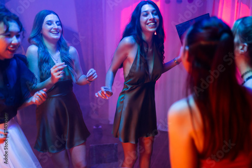 Energetic group of young women laughing and dancing at a lively party with colorful lights, creating an exciting and joyful atmosphere perfect for celebrations and social gatherings.