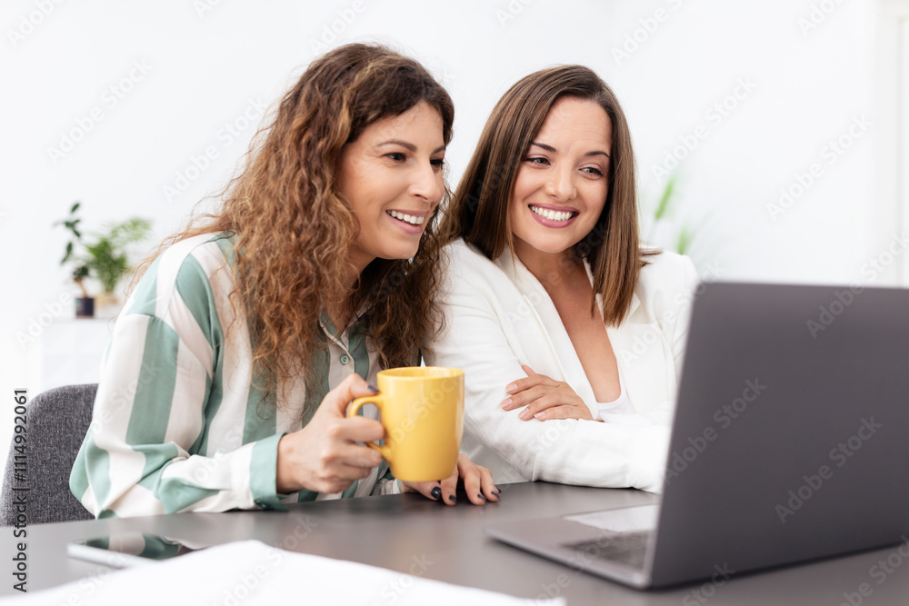 Two millennial businesswomen engage with a laptop in a modern office setting, sharing insights and ideas while enjoying their coffee. The atmosphere is casual yet focused. Two millennial businesswomen engage with a laptop in a modern office setting, sharing insights and ideas while enjoying their coffee. The atmosphere is casual yet focused.