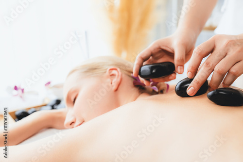 Hot stone massage at spa salon in luxury resort with day light serenity ambient, blissful woman customer enjoying spa basalt stone massage glide over body with soothing warmth. Quiescent
