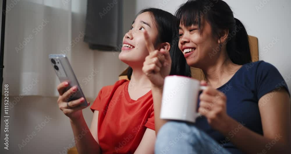 Handheld shot, Two Asian siblings sit on the floor, search for interior design ideas on their phone, and discuss decorating a room in new home. Moving and lifestyle concepts. Handheld shot, Two Asian siblings sit on the floor, search for interior design ideas on their phone, and discuss decorating a room in new home. Moving and lifestyle concepts.