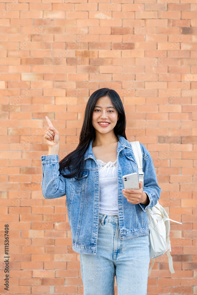 A smiling woman points at an empty space while standing outdoors with a brick wall in the background A smiling woman points at an empty space while standing outdoors with a brick wall in the background