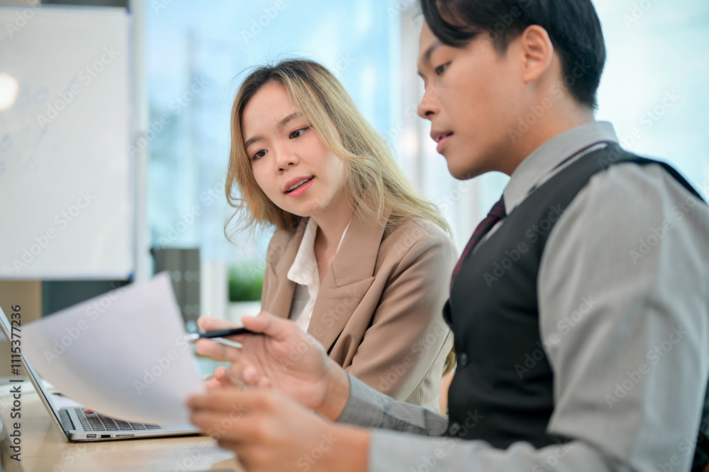 A beautiful Asian businesswoman sits in a meeting, focused on listening to her colleague's idea.