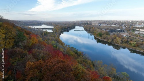 Aerial pull back shot of Mississippi river surrounded by fall colors near St Paul with cityscape of Minnesota at background in USA. photo