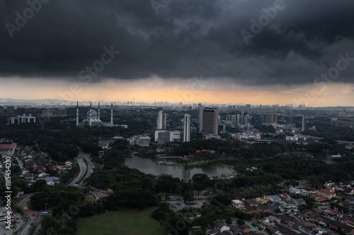 Dark and grey dramatic thunderstorm clouds over the big city with tall buildings and mosque in Asia. 