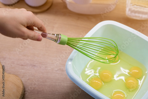 A hand whisking eggs in a plastic bowl